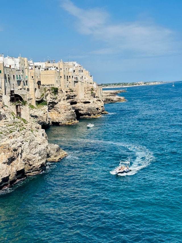 Un bateau longe les falaises de Polignano a Mare en direction des grottes.