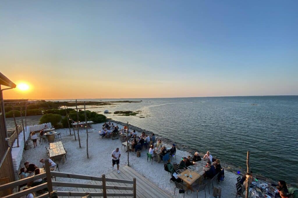 Des personnes en bord de mer lors du coucher de soleil sur la terrasse d'une cabane à huitres du bassin d'Arcachon