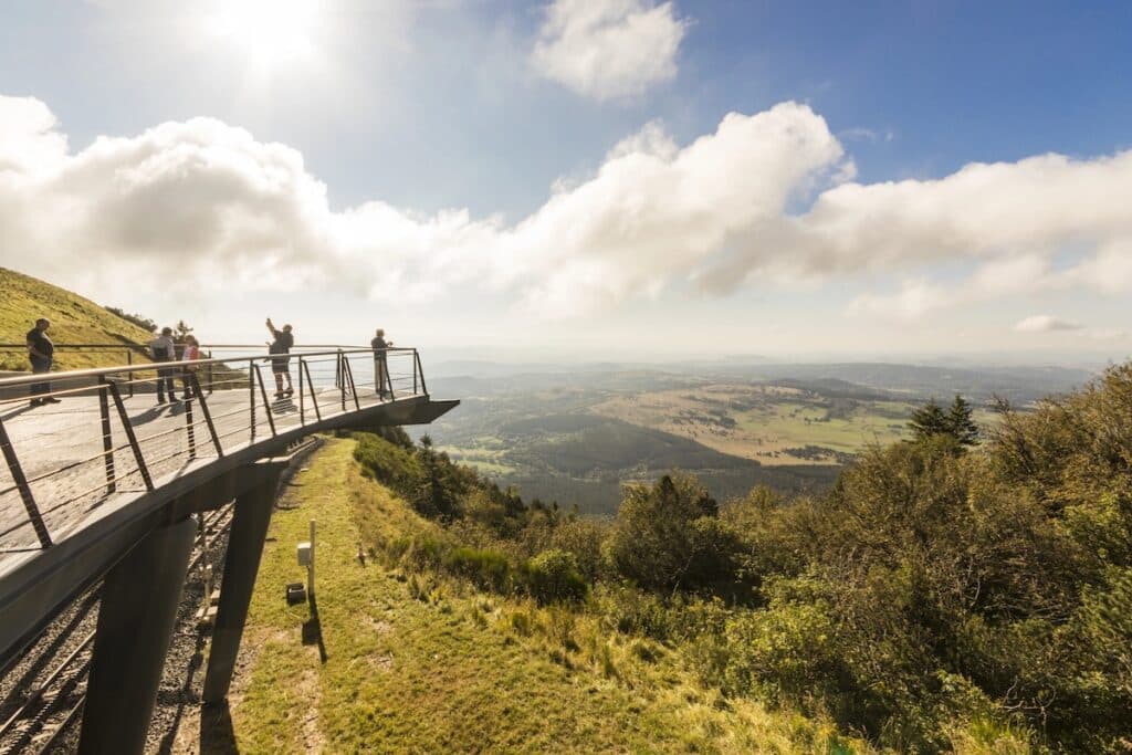 Des personnes admirent le panorama sur les volcans d'Auvergne depuis une passerelle au sommet du puy de Dôme