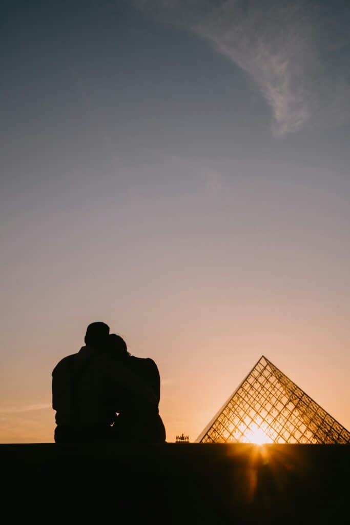 Un couple enlassé dmire la pyramide du Louvre en fin de journée.