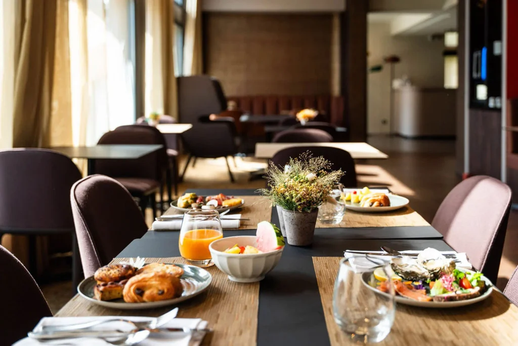 Tables dressées pour le petit-déjeuner au Masq Hôtel avec viennoiseries, jus d'orange, salade de fruits et assiette salée