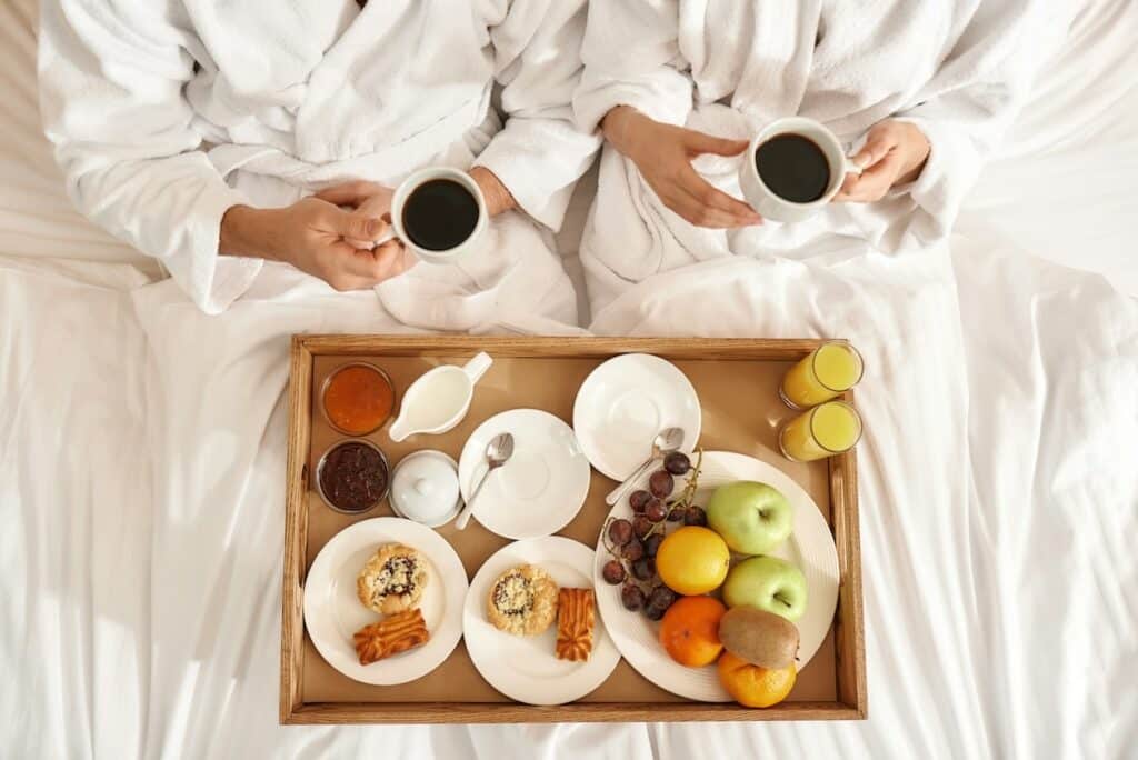 Un couple déguste un petit déjeuner sur le lit de leur chambre d'hôtel.