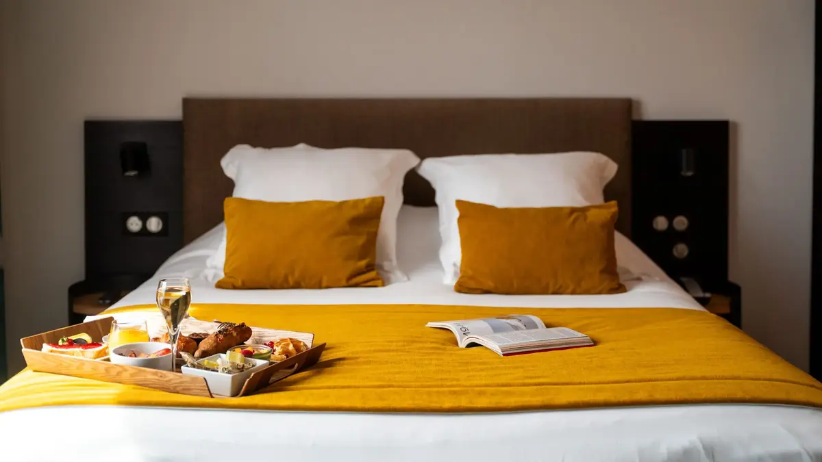 Chambre Cosy Double du Masq Hôtel avec jeté de lit moutarde et plateau de petit-déjeuner posé sur le lit