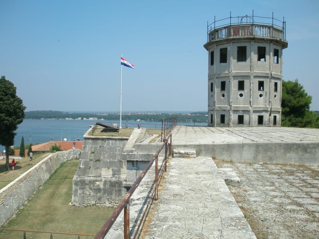 Remparts de la forteresse du Kaštel avec drapeau croate, tour d'observation et vue sur la baie de Pula