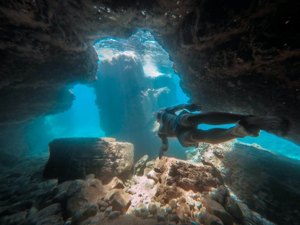 Nageur avec masque et tuba explorant une grotte sous-marine éclairée par la lumière de surface