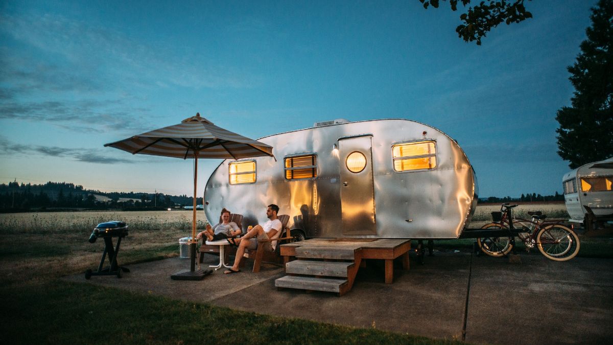 Deux personnes de nit au bord de leur caravane font du camping.