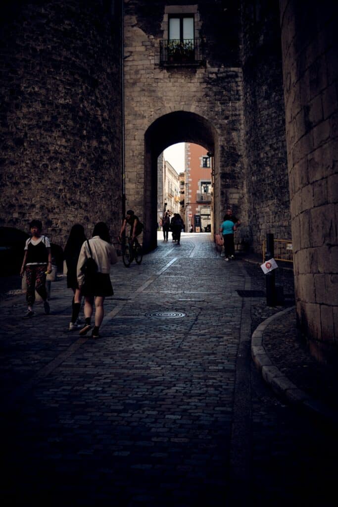 Des touristes remontent une rue médiévale proche d'une porte d'accès au bari vecchio à Gérone.