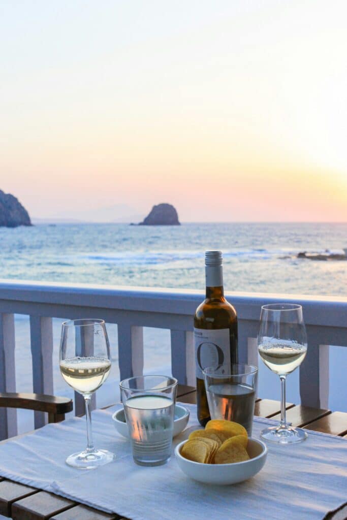 Une table d'un restaurant dressée avec une bouteille de vin, des verres et du pain avec vue sur la baie de Pollonia sur l'île de Milos.