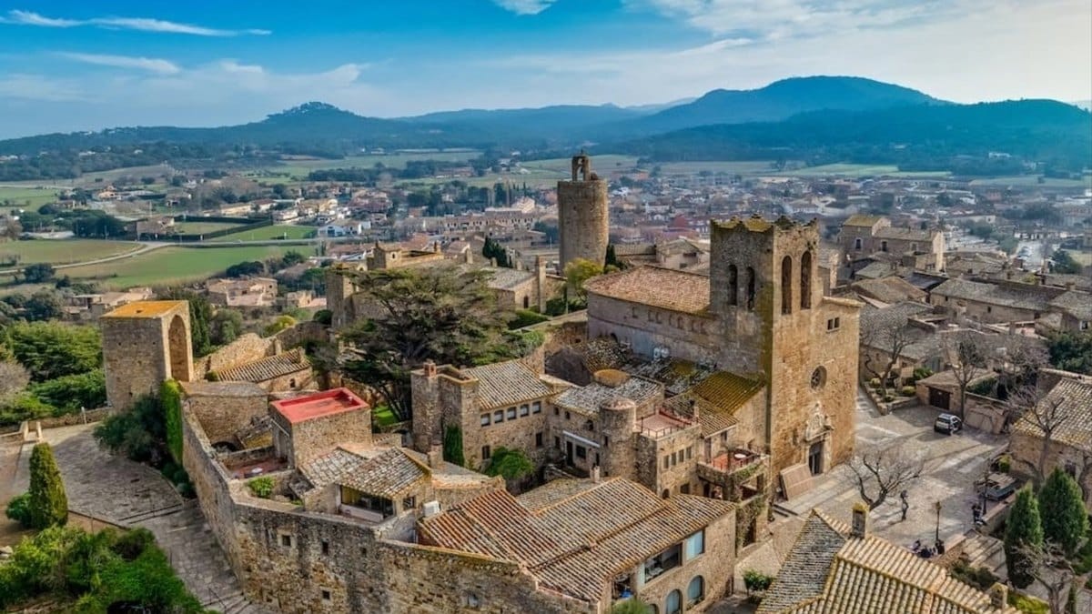 Vue aérienne du vieux Pals, l'église Sant Pere et la Torre de les Hores, avec la plaine de l'Empordà et les collines au fond