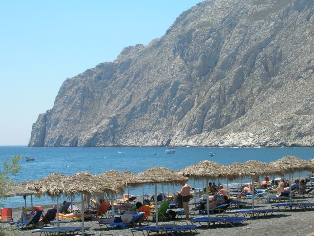 Transats et parasols alignés sur le sable noir volcanique de la plage de Kamari à Santorin