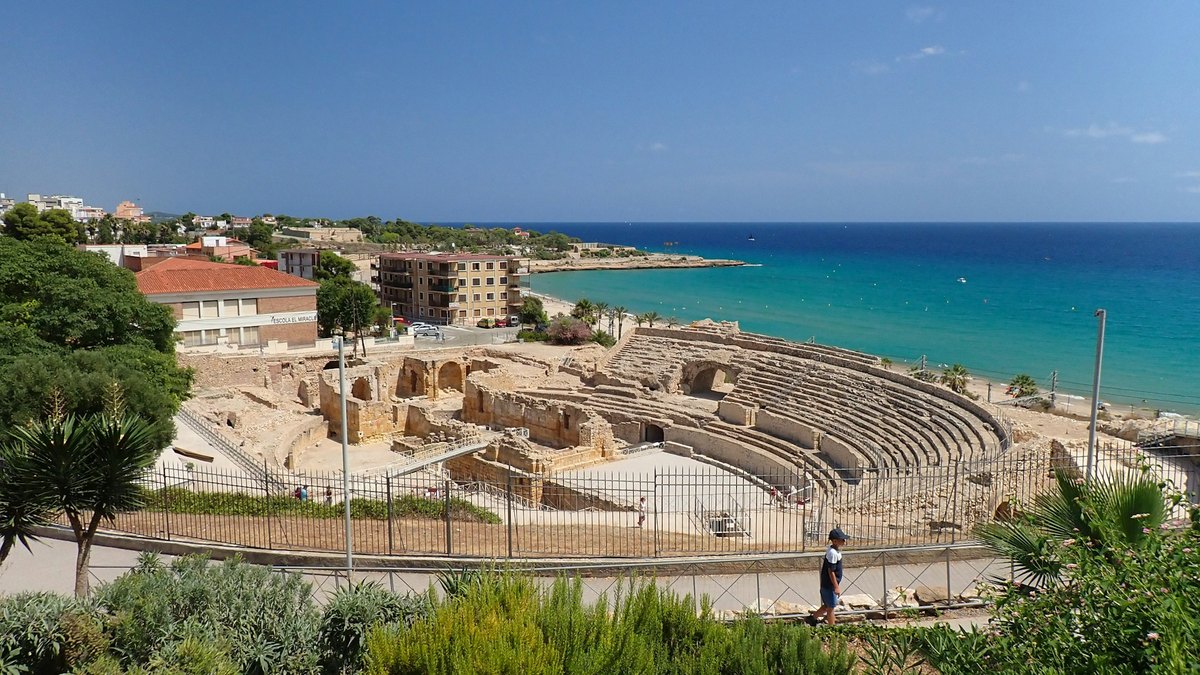 L'amphithéâtre romain de Tarragone et ses gradins au bord de la mer turquoise, entre palmiers et végétation