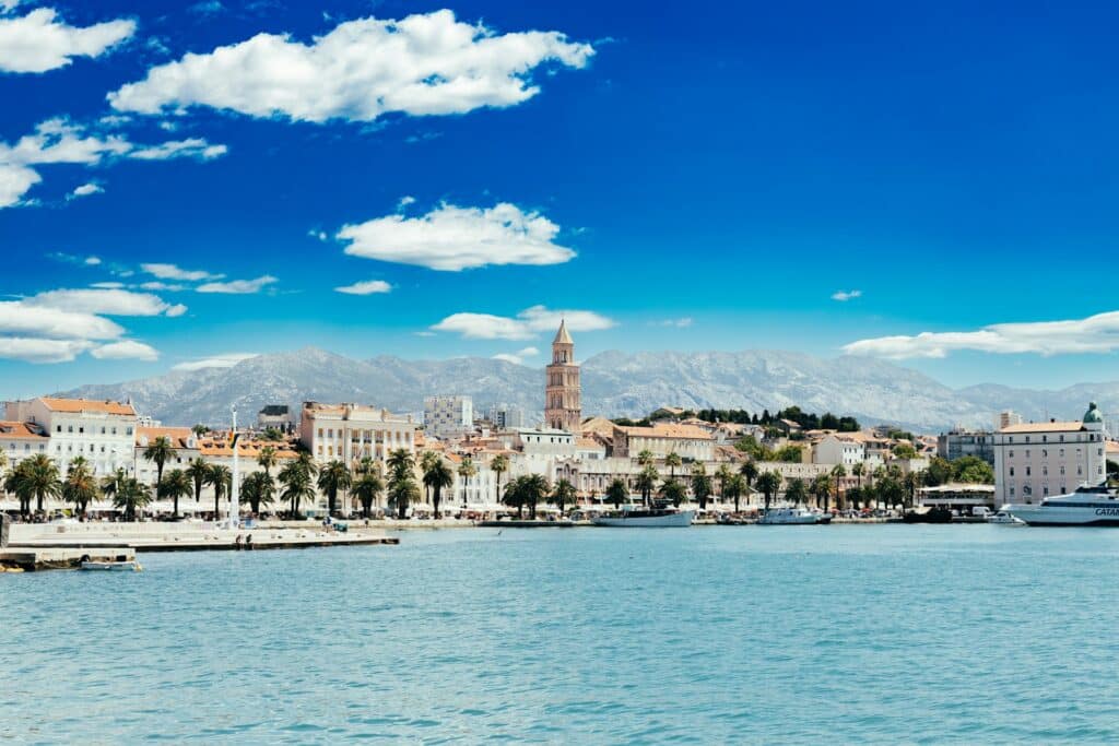 Promenade de la Riva bordée de palmiers face au port, avec le palais et le clocher de Saint-Domnius