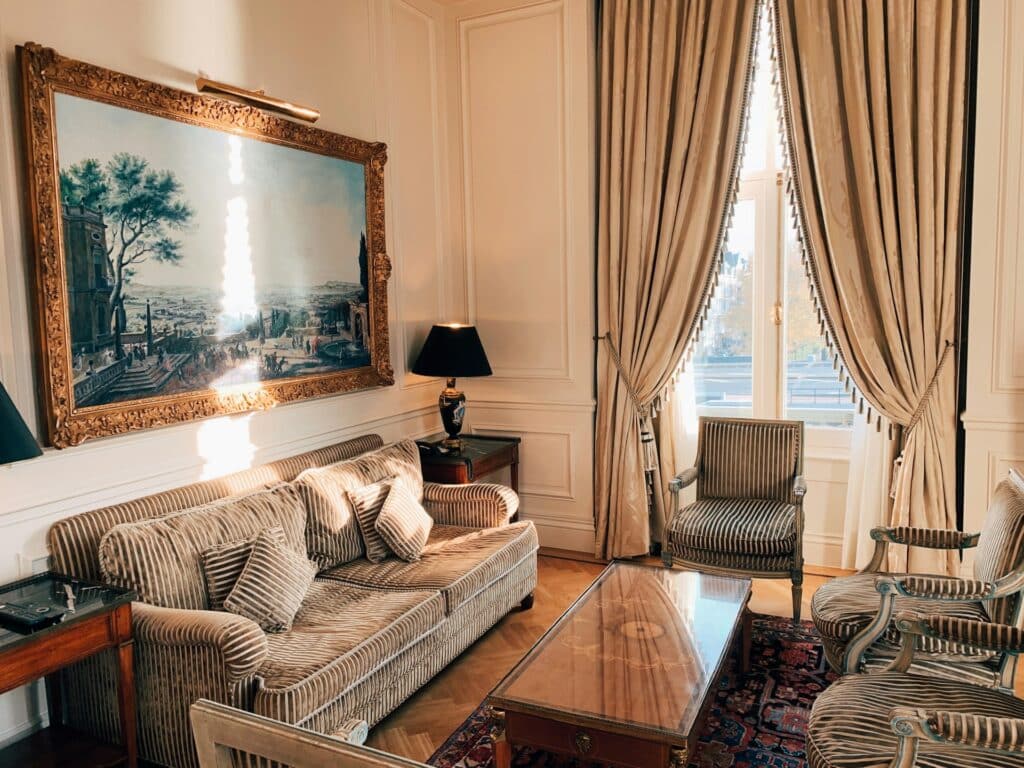 Salon d'une suite d'hôtel de style classique parisien avec canapé, moulures et hautes fenêtres