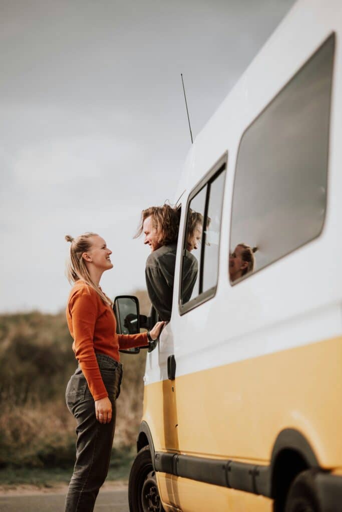 Couple de voyageurs devant leur van aménagé jaune et blanc
