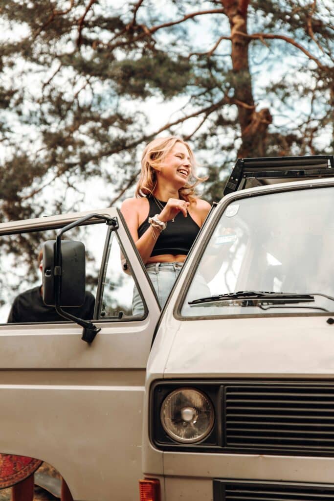 Voyageuse souriante dans son van vintage sous les pins landais