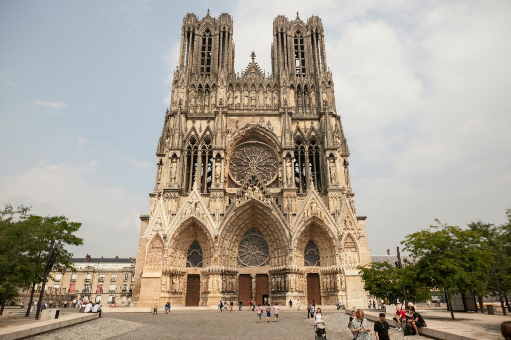 Des personnes se proménent devant la Cathédrale Notre-Dame de Reims au niveau de la place du Cardinal Luçon.