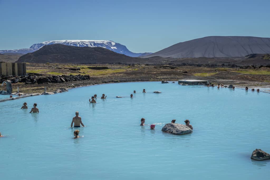 Des personnes se baignent en été dans les eaux chaudes du Myvatn Nature Baths en appréciant une vue spectaculaire sur la nature sauvage islandaise.